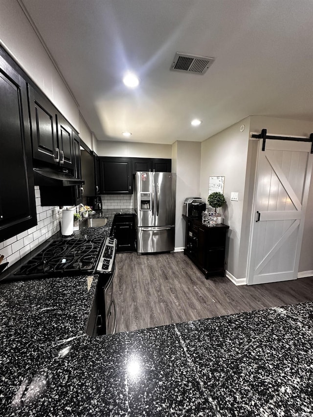 kitchen with stainless steel refrigerator with ice dispenser, tasteful backsplash, visible vents, a barn door, and dark cabinets