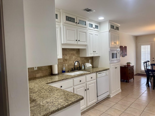 kitchen with white appliances, a sink, visible vents, white cabinets, and glass insert cabinets