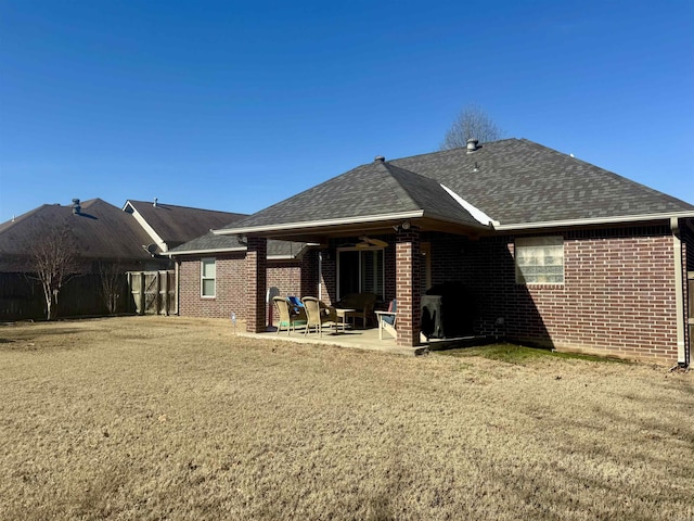 rear view of house featuring a shingled roof, a yard, a patio area, and brick siding