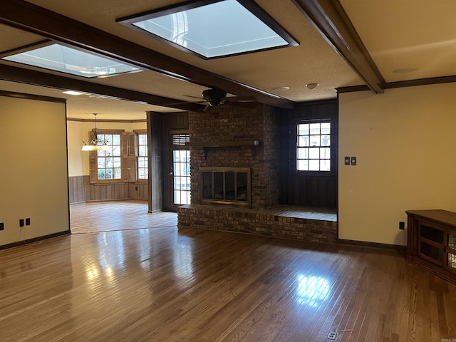 unfurnished living room with ceiling fan, wooden walls, wood finished floors, a brick fireplace, and beamed ceiling