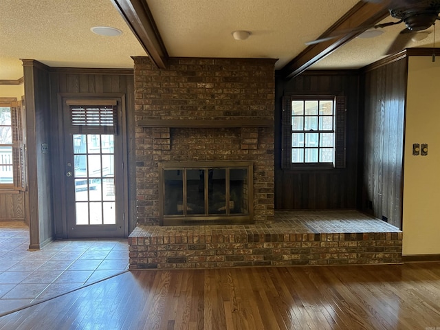 unfurnished living room with wooden walls, a textured ceiling, beam ceiling, and wood finished floors