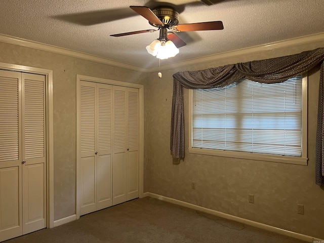 unfurnished bedroom with a textured ceiling, ceiling fan, carpet floors, multiple closets, and ornamental molding