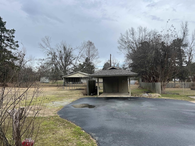 view of front facade featuring driveway, roof with shingles, fence, and a detached carport