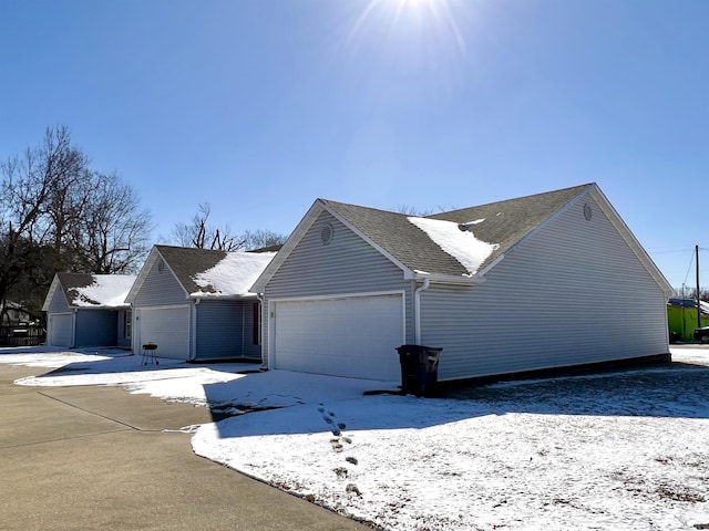 snow covered property with a garage and roof with shingles