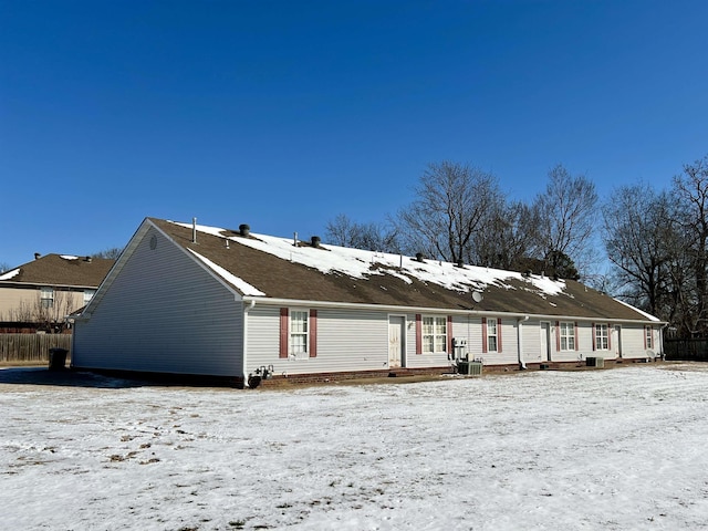 snow covered property featuring central AC unit and fence