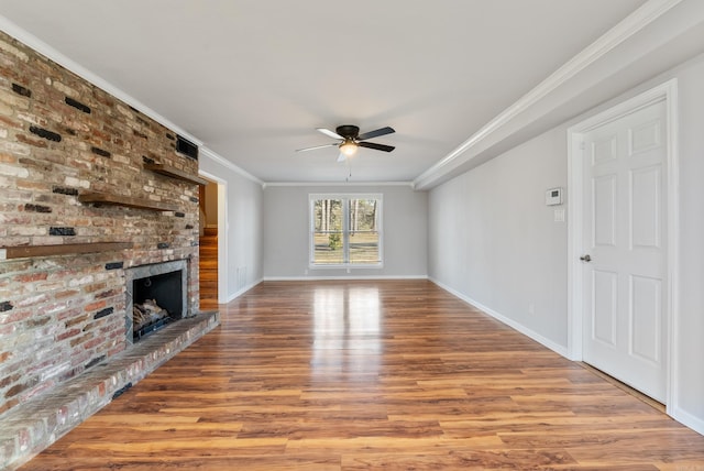 unfurnished living room featuring ceiling fan, wood finished floors, baseboards, a brick fireplace, and crown molding