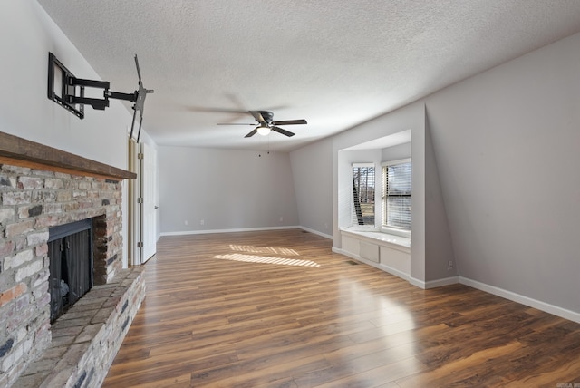 unfurnished living room with baseboards, a fireplace with raised hearth, dark wood finished floors, a ceiling fan, and a textured ceiling