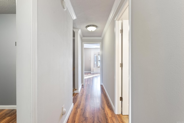 corridor with baseboards, a textured ceiling, ornamental molding, and wood finished floors