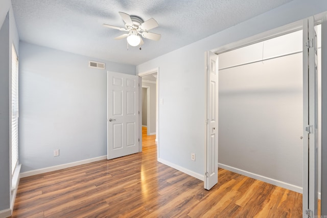 unfurnished bedroom featuring a closet, visible vents, a textured ceiling, wood finished floors, and baseboards