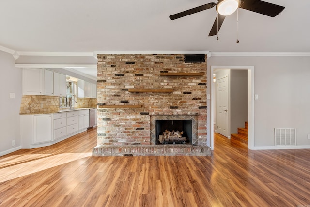 unfurnished living room with a brick fireplace, light wood-style flooring, visible vents, and crown molding