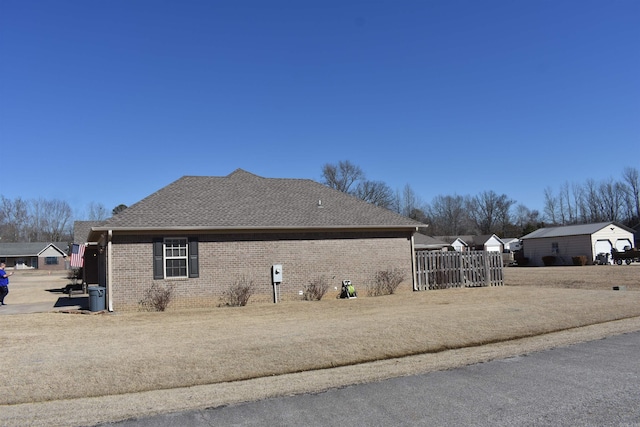 view of home's exterior featuring brick siding, roof with shingles, and fence