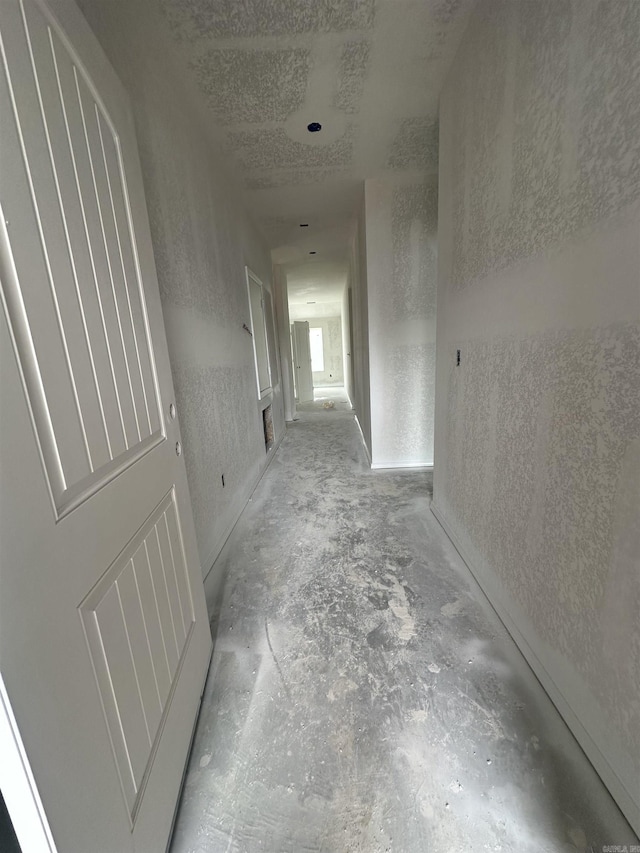 corridor with unfinished concrete floors, a textured ceiling, and a textured wall