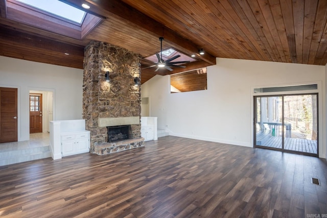 unfurnished living room featuring a skylight, baseboards, visible vents, dark wood-type flooring, and a stone fireplace