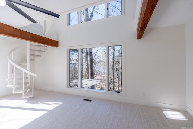 unfurnished living room with carpet floors, beam ceiling, visible vents, and a healthy amount of sunlight