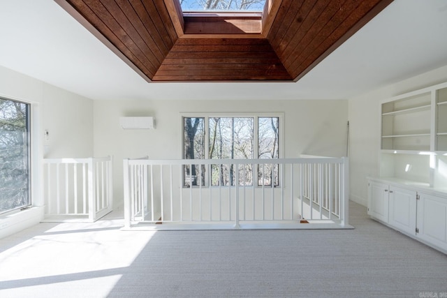 interior space with a skylight, a raised ceiling, light colored carpet, wood ceiling, and a wall mounted air conditioner