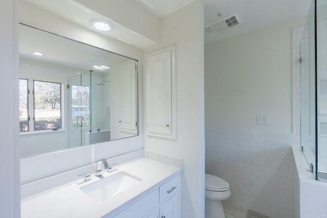 full bath with visible vents, wainscoting, toilet, vanity, and tile walls