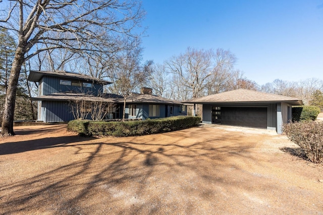 view of front facade with a garage, a chimney, and dirt driveway