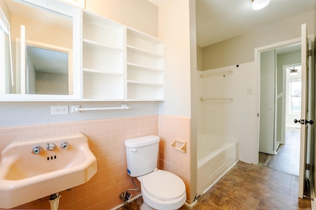 bathroom with a bathtub, a wainscoted wall, tile walls, toilet, and a sink