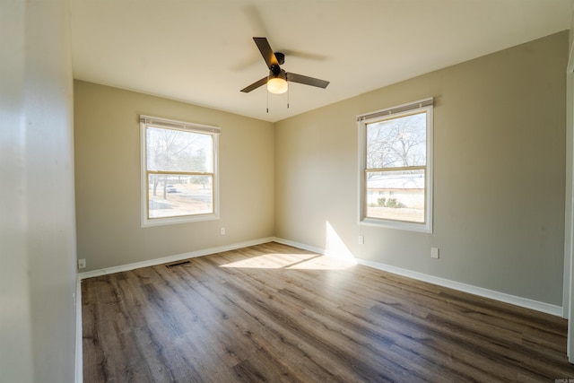 empty room featuring a ceiling fan, a wealth of natural light, dark wood-style flooring, and baseboards