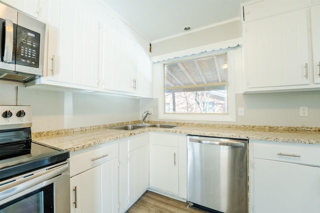 kitchen featuring light wood finished floors, appliances with stainless steel finishes, white cabinetry, a sink, and light stone countertops