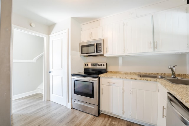 kitchen featuring stainless steel appliances, white cabinetry, a sink, and light wood finished floors