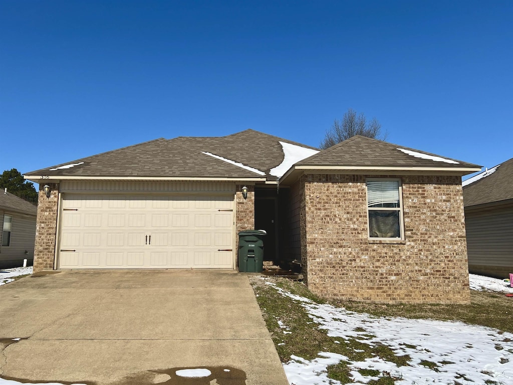 ranch-style house with a garage, concrete driveway, brick siding, and roof with shingles