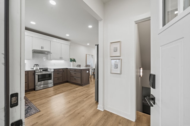 kitchen featuring under cabinet range hood, white cabinets, light countertops, light wood finished floors, and stainless steel range with electric stovetop