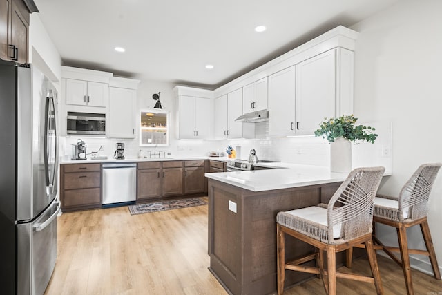 kitchen featuring stainless steel appliances, a breakfast bar, light countertops, and a peninsula