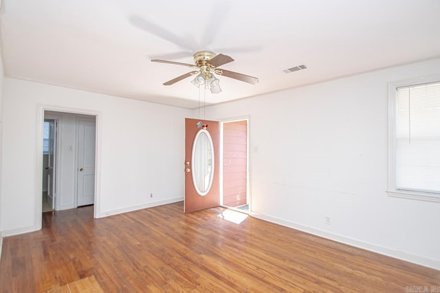 empty room with dark wood-style floors, visible vents, baseboards, and a ceiling fan