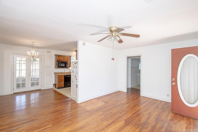 unfurnished living room with ceiling fan with notable chandelier, light wood-type flooring, baseboards, and wallpapered walls