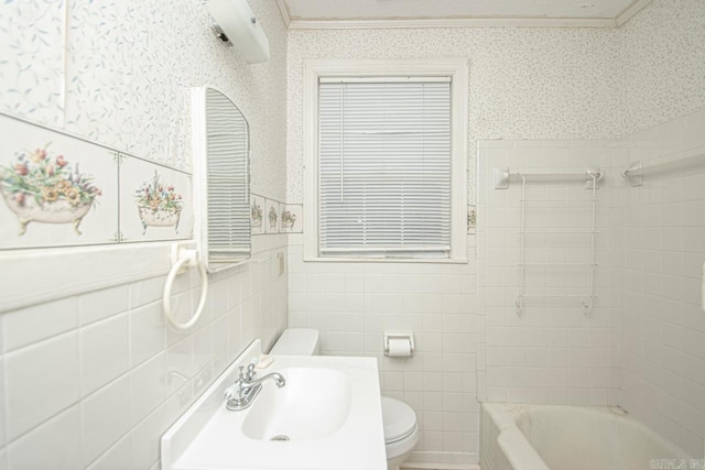 bathroom with a tub to relax in, tile walls, toilet, a sink, and wallpapered walls