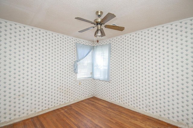 empty room with wallpapered walls, a textured ceiling, baseboards, and wood finished floors