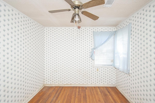 spare room with wood finished floors, visible vents, a textured ceiling, and wallpapered walls