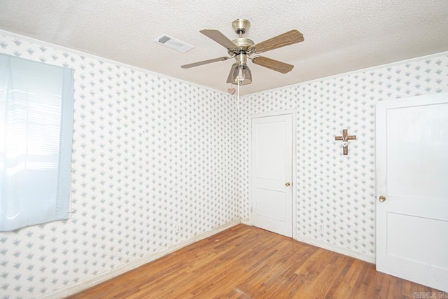 empty room featuring wallpapered walls, visible vents, a ceiling fan, wood finished floors, and a textured ceiling