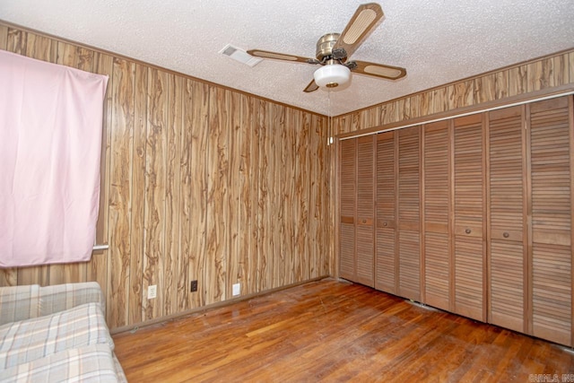 unfurnished bedroom featuring a textured ceiling, ceiling fan, wood walls, wood finished floors, and crown molding