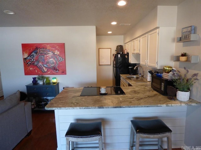 kitchen featuring a peninsula, a sink, a kitchen breakfast bar, white cabinets, and black appliances