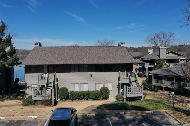 view of front of house with uncovered parking, stairway, a chimney, and roof with shingles