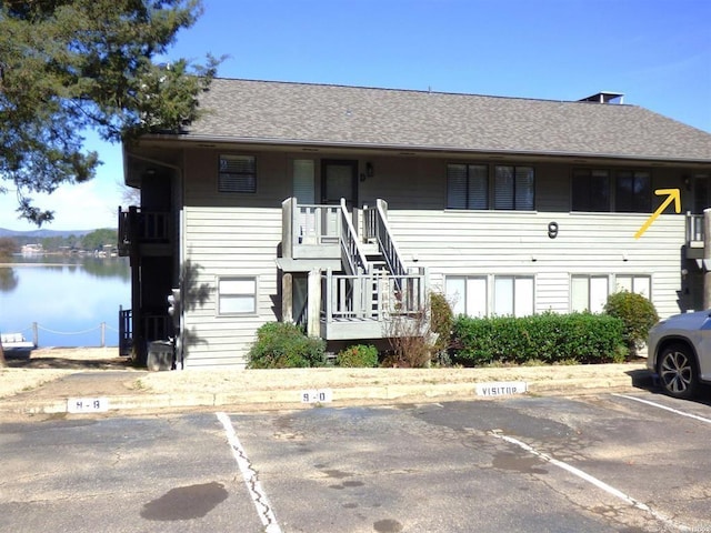 view of property featuring uncovered parking, a shingled roof, and a water view