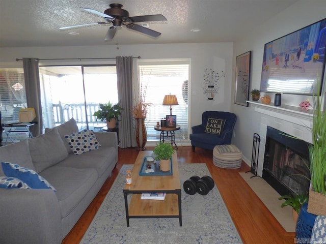 living area with a fireplace with flush hearth, ceiling fan, a textured ceiling, and wood finished floors