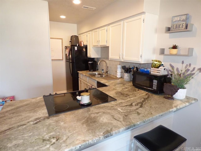 kitchen featuring tasteful backsplash, light stone counters, black appliances, white cabinetry, and a sink