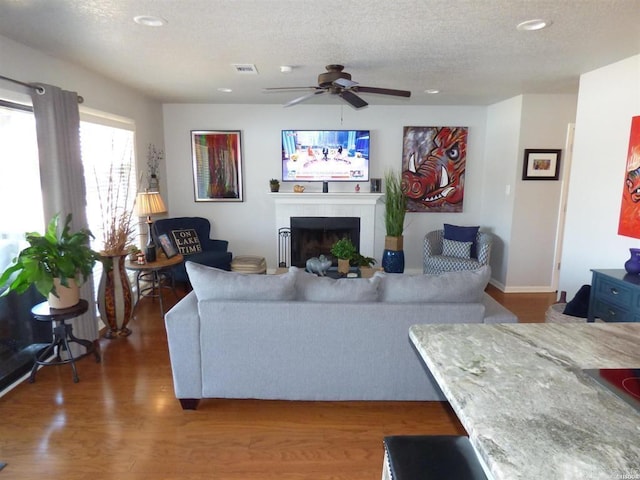 living area with visible vents, a tiled fireplace, ceiling fan, wood finished floors, and a textured ceiling