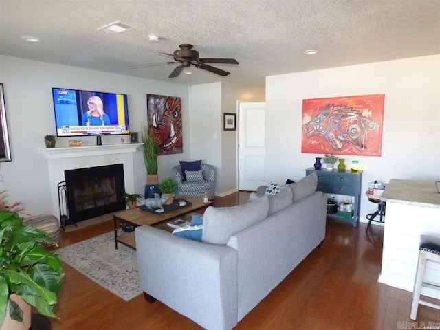 living area with ceiling fan, a textured ceiling, dark wood finished floors, and a tiled fireplace