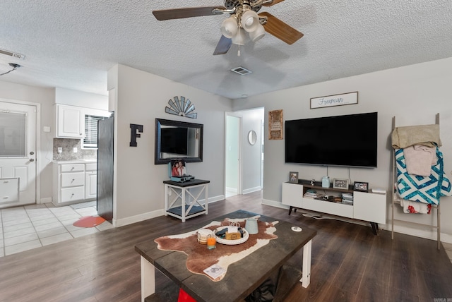 living area featuring a ceiling fan, a textured ceiling, visible vents, and wood finished floors