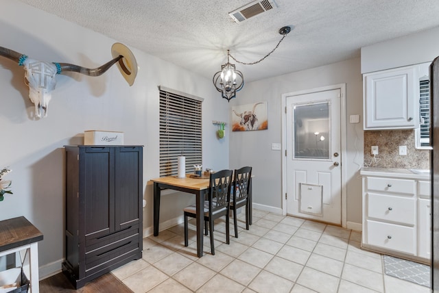 dining area with light tile patterned floors, baseboards, visible vents, a textured ceiling, and a notable chandelier