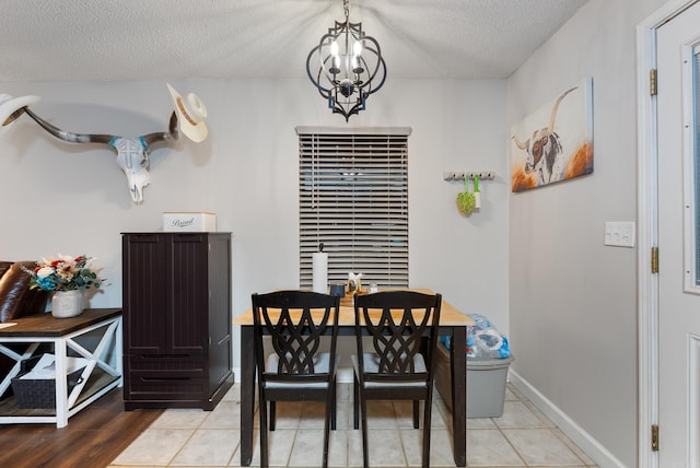 dining space with light tile patterned floors, a textured ceiling, baseboards, and a notable chandelier