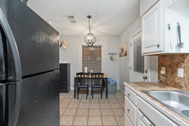 kitchen featuring pendant lighting, visible vents, freestanding refrigerator, white cabinets, and a sink