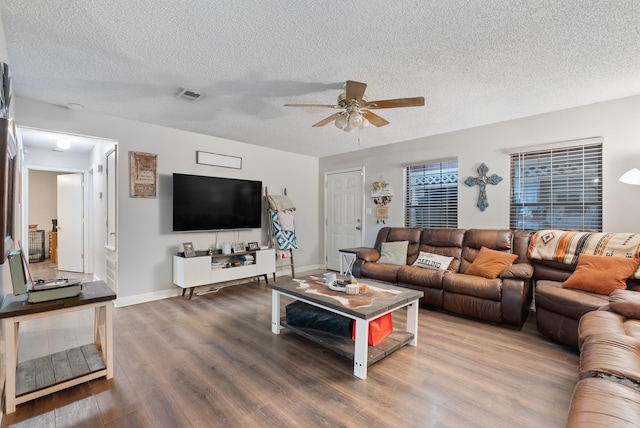 living room with a textured ceiling, wood finished floors, visible vents, baseboards, and a ceiling fan