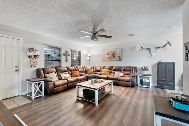 living area with a ceiling fan, visible vents, dark wood finished floors, and a textured ceiling