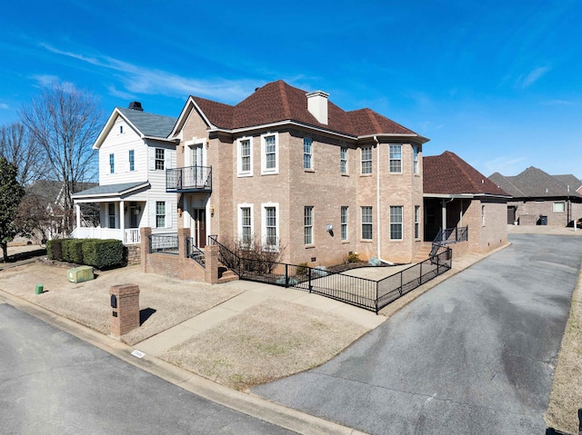 view of front of property with a fenced front yard, a chimney, roof with shingles, covered porch, and brick siding