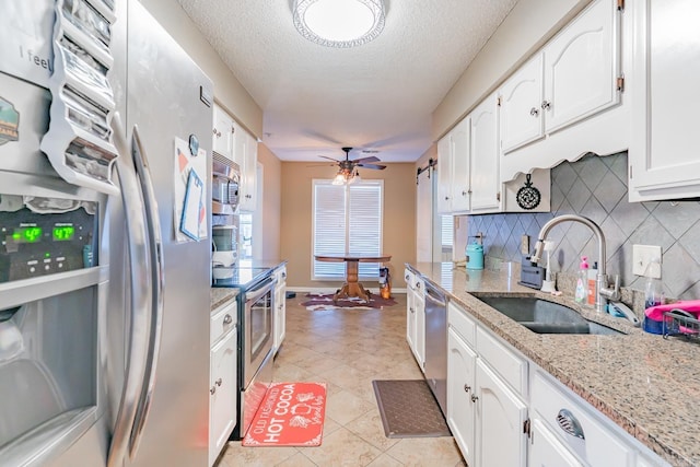 kitchen featuring light stone countertops, stainless steel appliances, a sink, white cabinets, and decorative backsplash